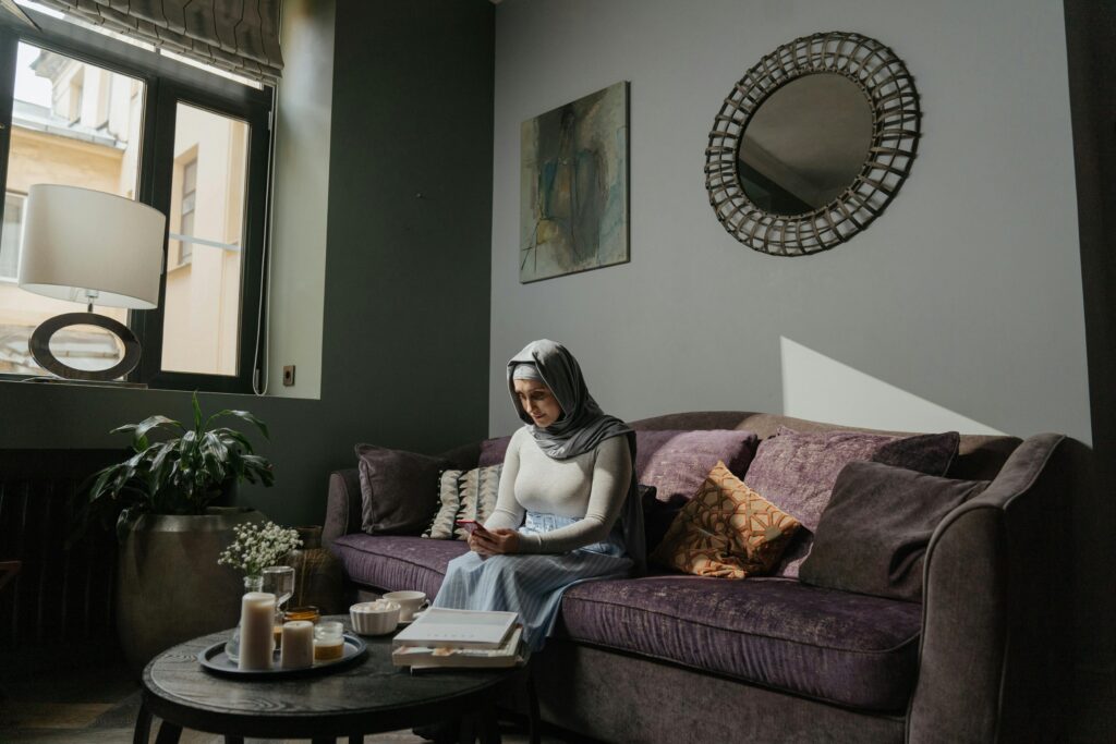 A woman in traditional hijab reads in a cozy living room with stylish decor and natural lighting.